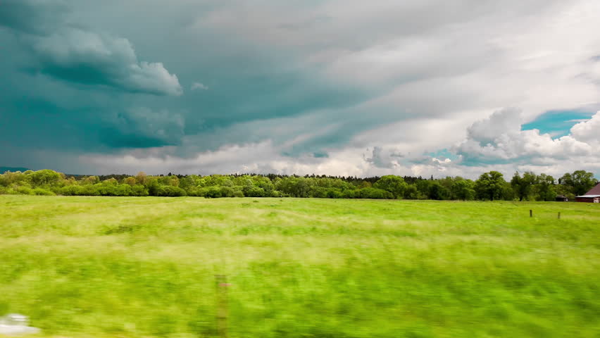 Dynamic view of a wide green field and dark storm clouds rolling in, captured from a moving vehicle. Powerful contrast between lush grass and dramatic sky. Perfect for nature, travel, weather, and