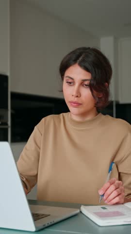 Latin freelance businesswoman woman entrepreneur using computer online remote business studying writing notes. Concentrated young hispanic female girl student working on laptop pc at home. Vertical