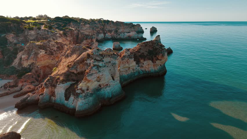 A captivating aerial perspective showcases rugged coastal cliffs against the serene blue waters of the Atlantic Ocean near Lagos, Portugal, highlighting natural beauty.
