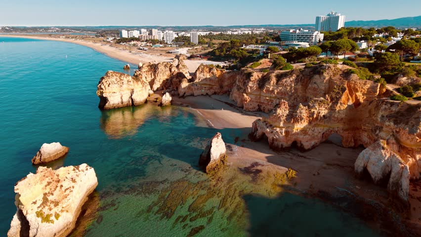 A breathtaking aerial perspective showcases the rugged coastline of Algarve, Portugal, featuring golden cliffs, clear blue waters, and sandy beaches at sunset.