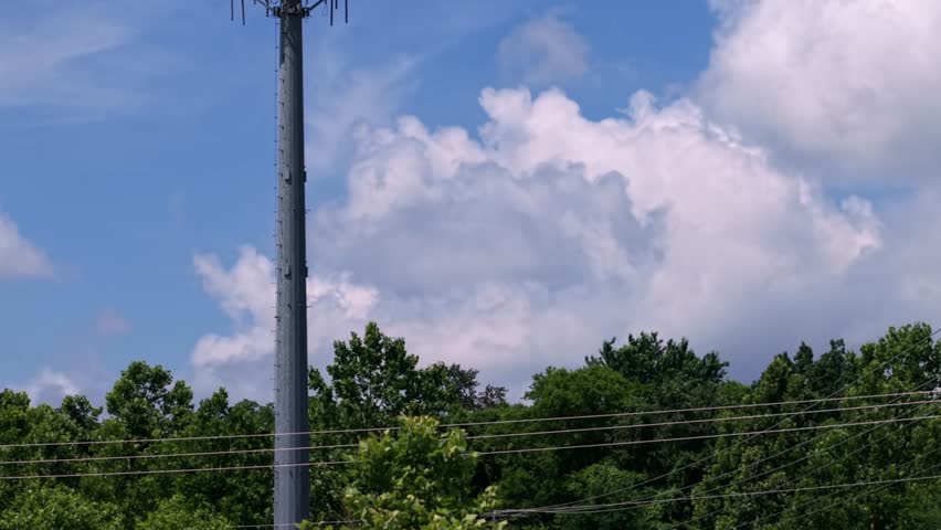 Cellular microwave signal antenna tower - aerial reveal rising above the trees in front of clouds