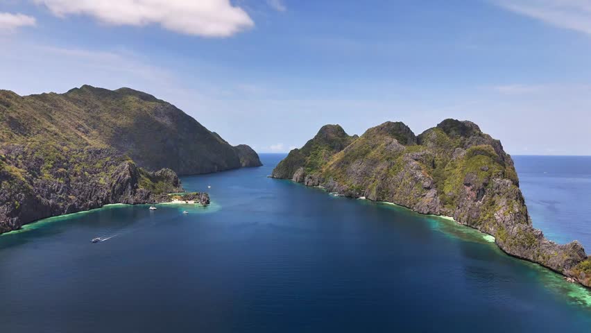 Aerial view of Star Beach on Tapiutan Island in the Philippines with deep blue waters, cliffs, and boats anchored near coral reefs along the lush coastline under clear blue skies