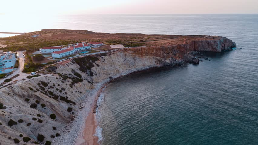 An aerial perspective captures a beautiful coastal area in Portugal, showcasing cliffs, sandy beaches, and calm waters under a fading sunset sky.