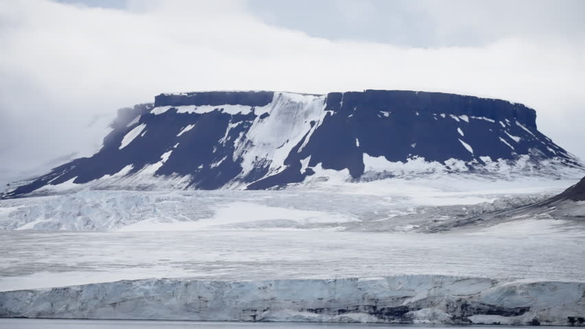 A majestic flat-topped mountain rises above a stark, frozen landscape, surrounded by icy plains and dramatic clouds in an untouched arctic wilderness.