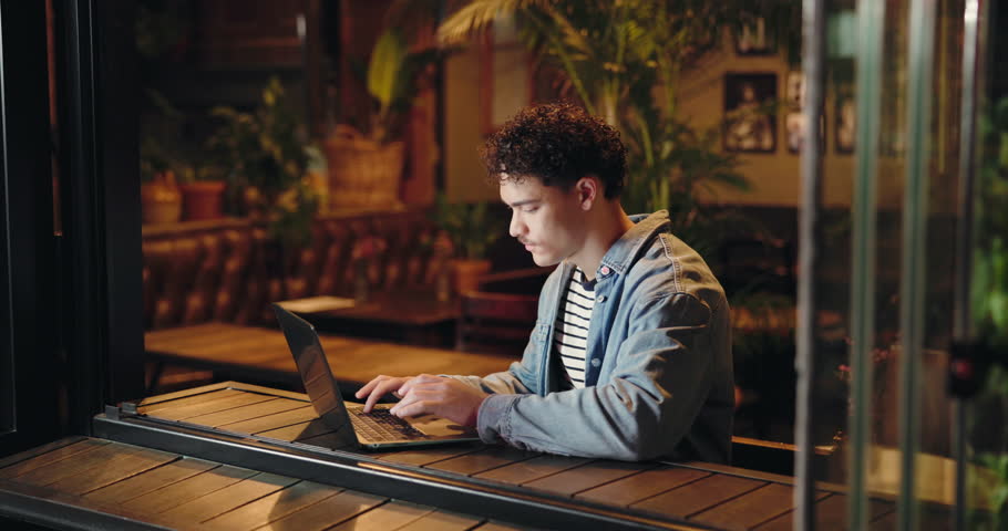 Remote work, night and man in cafe with laptop, typing email or project draft with connection. Creative writer, computer or productivity in coffee shop for business blog, article deadline or research