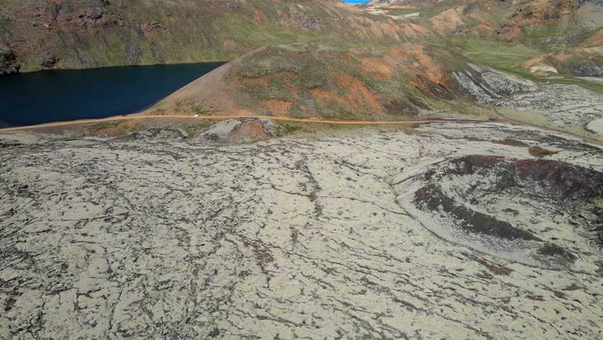 Aerial view of the contrasting textures of the dark blue lake against the pale, cracked earth, with mountains in the background, Grindavik, Grindavíkurbaer, Iceland.