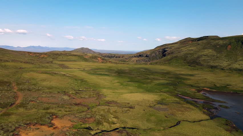 Aerial view of lush green mountains meeting calm blue lakes under a clear sky, creating a serene and untouched landscape, Hveragerði, Sveitarfélagið Olfus, Iceland.