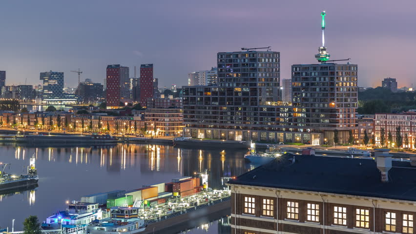 Aerial view over towers in Maashaven night to day transition timelapse with moored ships, Katendrecht and Maas River, Rotterdam before sunrise. Illuminated factory converted to office and event space