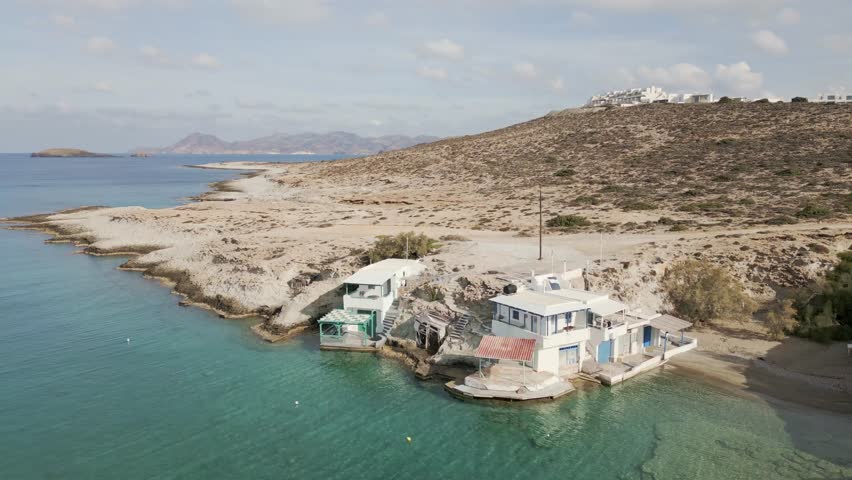 Aerial view of turquoise waters meeting a rugged coastline, with buildings nestled against the arid landscape, creating a striking contrast, Milos, Anatoliki Attiki, Greece.