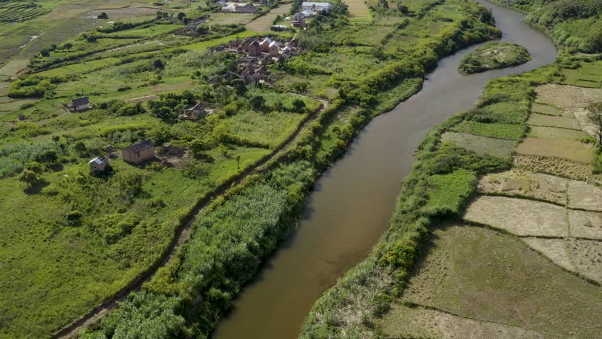 Aerial view of a river winding through the lush green valley, contrasting with the houses and agricultural fields, Ambodilendemy, Amoron'i Mania, Madagascar.