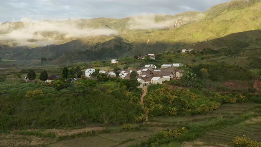 Aerial view of houses nestled amid green hills, with mist-shrouded mountains in the distance, a tranquil scene, Ambodilendemy, Amoron'i Mania, Madagascar.