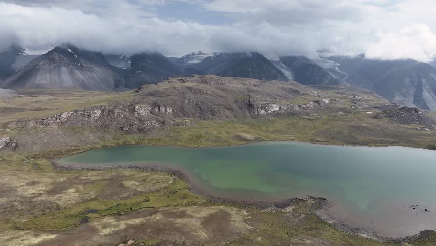 Aerial view of a serene lake nestled amongst rugged mountains, a contrast of turquoise waters against the gray and green landscape, Issyk-Kul, Kyrgyzstan.