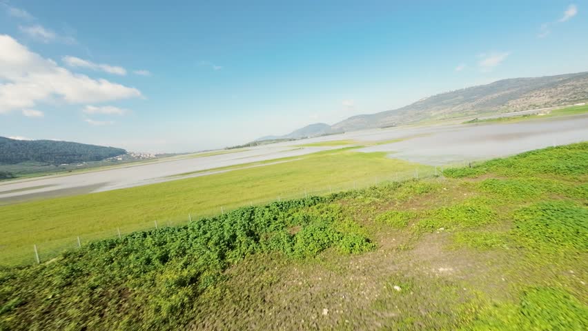 Aerial view of the serene Biq`at Bet Netofa landscape, where vibrant green meadows meet the tranquil waters under a vast blue sky, Biq`at Bet Netofa, Israel.