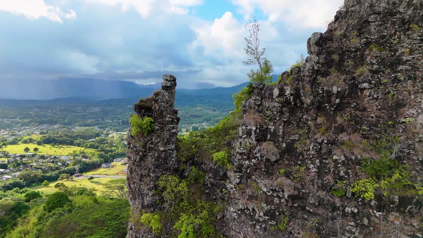 Aerial view of lush green fields meet distant mountains under a cloudy sky, showcasing Wailua