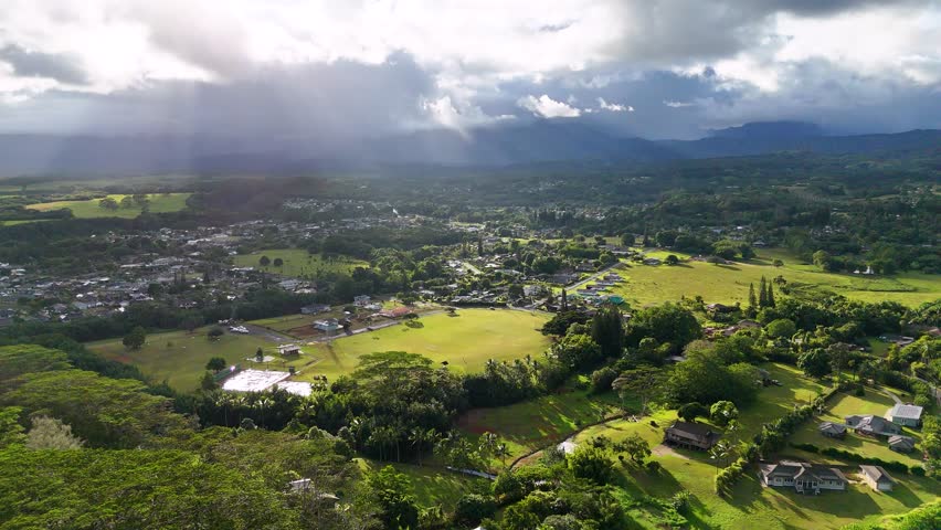 Aerial view of a lush green landscape with mountains in the background and sunlight breaking through the clouds, Wailua, Hawaii, United States.