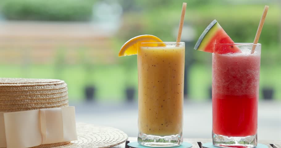 Refreshing summer drinks with citrus and watermelon garnishes in garden setting, straw hat beside glasses. Perfect for tropical, outdoor relaxation and healthy beverage concepts.