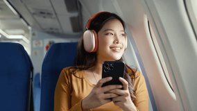 Young female passenger wearing wireless headphones scrolling smartphone while sitting by airplane window, enjoying in flight entertainment during leisure travel - Powered by Shutterstock - Get 15% off with code: PIKWIZARD15