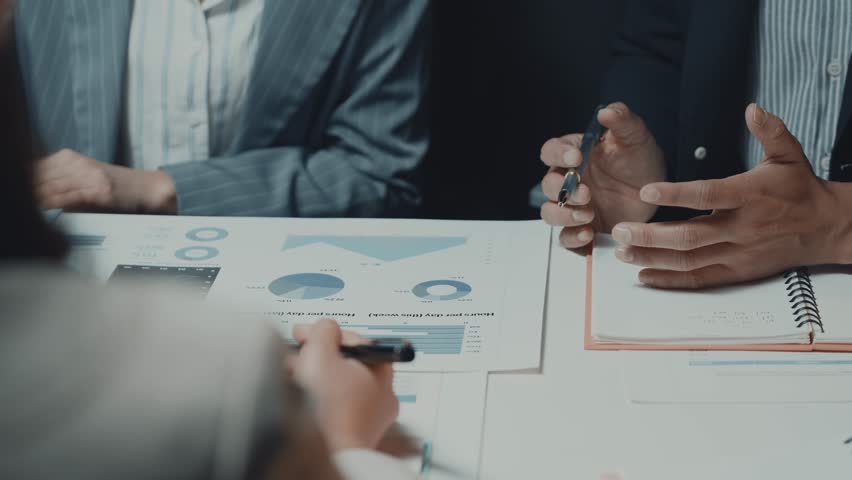 Business professionals collaborating on financial charts, intently analyzing data and taking detailed notes during strategic meeting at modern office workspace