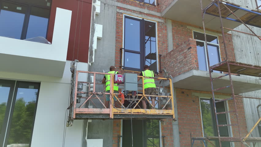 Construction Workers Ascending on Lift Platform, Mid-rise building facade installation in progress with safety gear