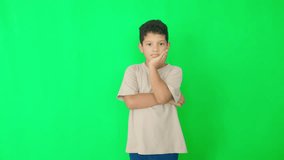 A young boy is standing in front of a green wall, looking down - Powered by Shutterstock - Get 15% off with code: PIKWIZARD15
