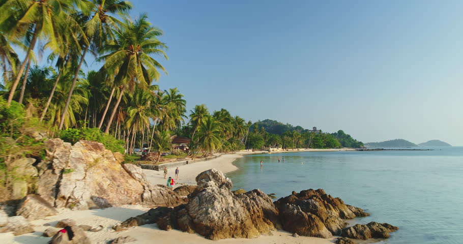Lush palm trees are leaning over a rocky tropical beach with white sand in Koh Samui, Thailand, creating a serene and idyllic paradise scene