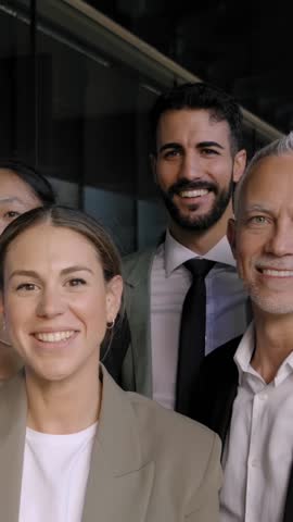 Vertical. Diverse multiracial group business people standing in office hallway looking cheerful at camera. Colleagues pose celebrating success by raising hands at same time and smiling happy together