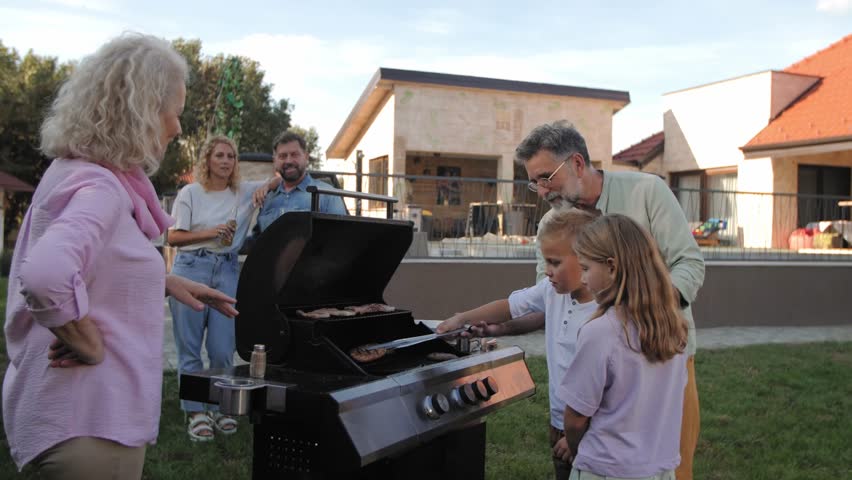Multigenerational family bonding while grandfather teaching grilling techniques to granddaughter in sunny backyard, family members watching closely