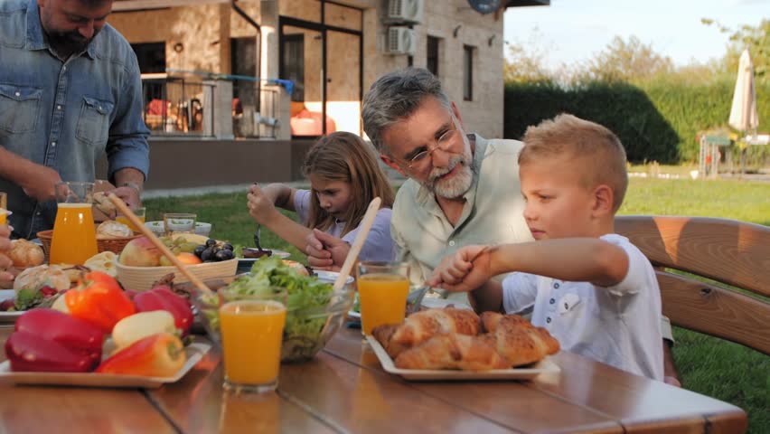 Multigenerational family enjoying sunny outdoor lunch, sharing delicious meal and laughter in garden setting with grandparents, parents, and children