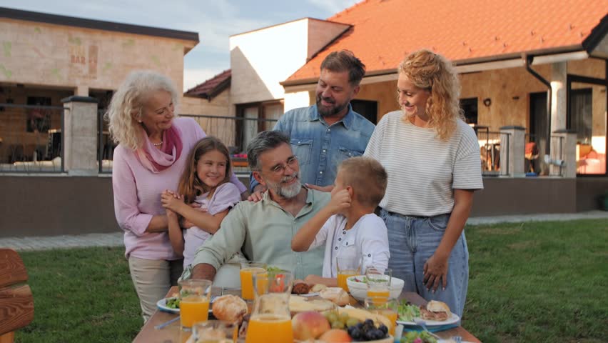 Happy multigenerational family posing for camera, enjoying food and good company in their backyard