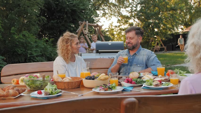 Elderly grandmother capturing heartwarming family moments during outdoor midday meal, creating lasting memories with smartphone photography in sunny backyard setting