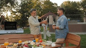 Two men are sharing drinks and conversation at a backyard barbecue, surrounded by food and friends - Powered by Shutterstock - Get 15% off with code: PIKWIZARD15