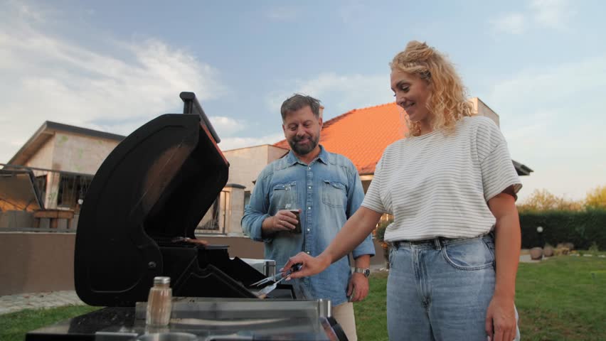 Happy couple preparing barbecue in their backyard, grilling meat and having fun on a sunny day