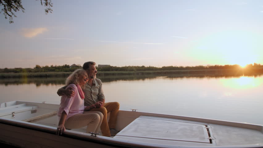 Mature couple sharing tender moment while sitting closely, embracing during golden hour sunset over tranquil lake waters, reflecting peaceful retirement lifestyle - Powered by Shutterstock - Get 15% off with code: PIKWIZARD15