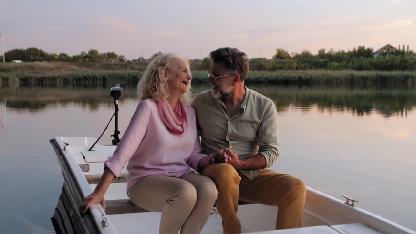 Senior couple sharing tender moment while holding hands, enjoying romantic boat ride during golden sunset light on tranquil water surface - Powered by Shutterstock - Get 15% off with code: PIKWIZARD15