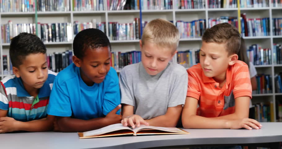 boys leaning over storybook at library table, initiating educational reading and flipping pages. Collaboration, learning, literature, education, diversity, teamwork, concentration