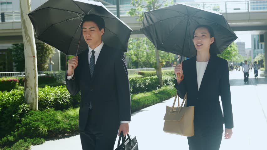 Male and female business people walking with parasols