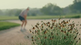 Shallow focus shot of flowers in the foreground while a male golfer hits out of a bunker in the blurred background. Captured in slow motion, the clip highlights contrast between beauty and action. - Powered by Shutterstock - Get 15% off with code: PIKWIZARD15