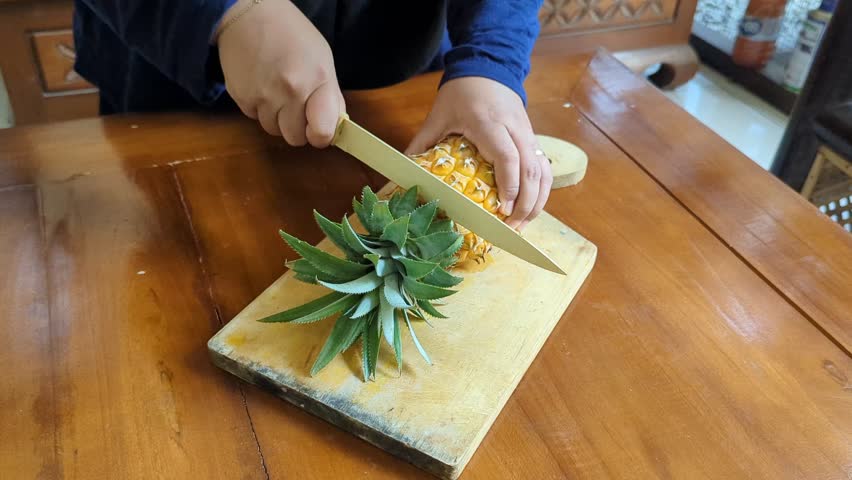 Closeup of a hand Women cut of peeled ripe pineapple on the wooden cutting board in kitchen, sweet delicious yellow pineapple cut into pieces. 4K Video
