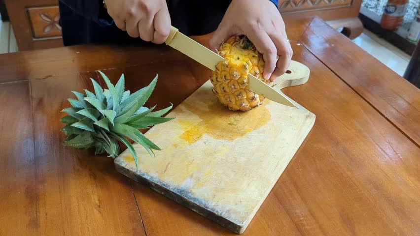 Closeup of a hand Women cut of peeled ripe pineapple on the wooden cutting board in kitchen, sweet delicious yellow pineapple cut into pieces. 4K Video