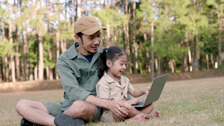Asian adult father and daughter using laptop together sitting on grass in forest park concentrating during digital learning time on peaceful family vacation day bonding through technology outdoors - Powered by Shutterstock - Get 15% off with code: PIKWIZARD15