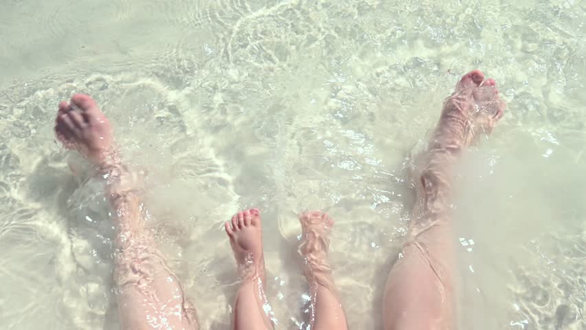 Top view of the legs of a one year old boy and his mother on the seashore. 