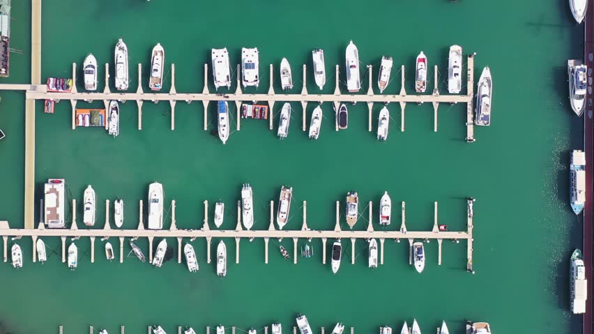 Experience the beauty of Qingdao's coastline where a yacht is anchored by the beach. This aerial view captures the vibrant harbor filled with various boats and the serene waters.