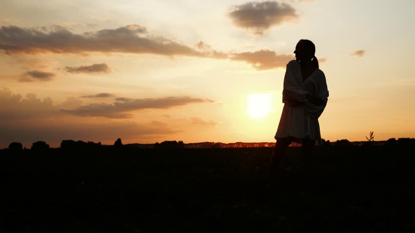 Silhouette of a young happy girl dancing at sunset with her arms outstretched at sunset in a field. The woman enjoys life and a beautiful summer sunset.