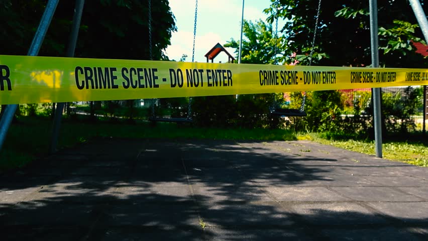 Scary and sad low angle footage of yellow colored vibrant Crime Scene Do Not Enter tape in front of two empty swings swinging at a playground showing that something has happened with a child. daytime.