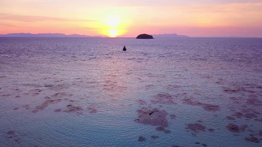 The sun sets over a tranquil sea with a distant island