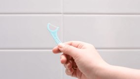 Female hand holding disposable dental floss close-up against the background of white tiles in the bathroom. - Powered by Shutterstock - Get 15% off with code: PIKWIZARD15