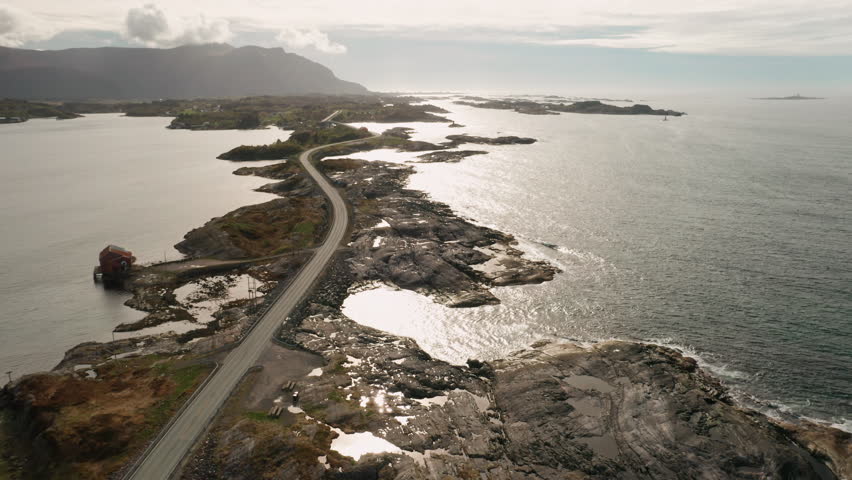 Atlantic ocean road curves gracefully along coastline connecting numerous islands. Rugged shore and vast expanse of ocean under cloudy sky at twilight