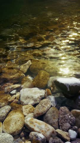 A clear stream glides smoothly over polished pebbles in golden light.