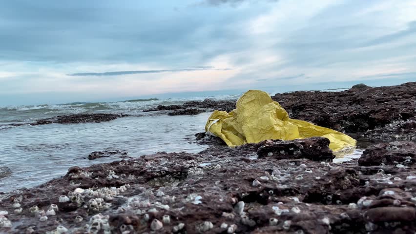 yellow plastic bag on rocky ocean shore. ecological problem of mankind. environmental pollution