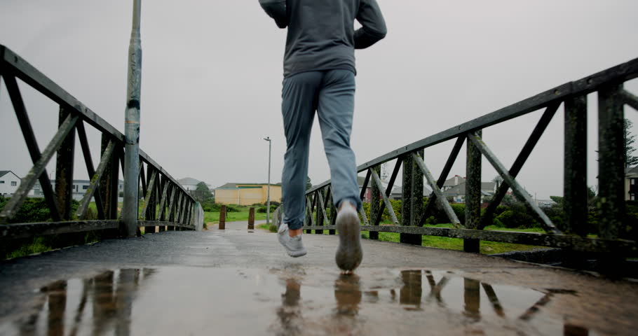 Running, back and health with legs of man in city for winter, marathon practice and fitness. Wellness, exercise and sports workout with person training on bridge for resilience, rain puddle or cardio